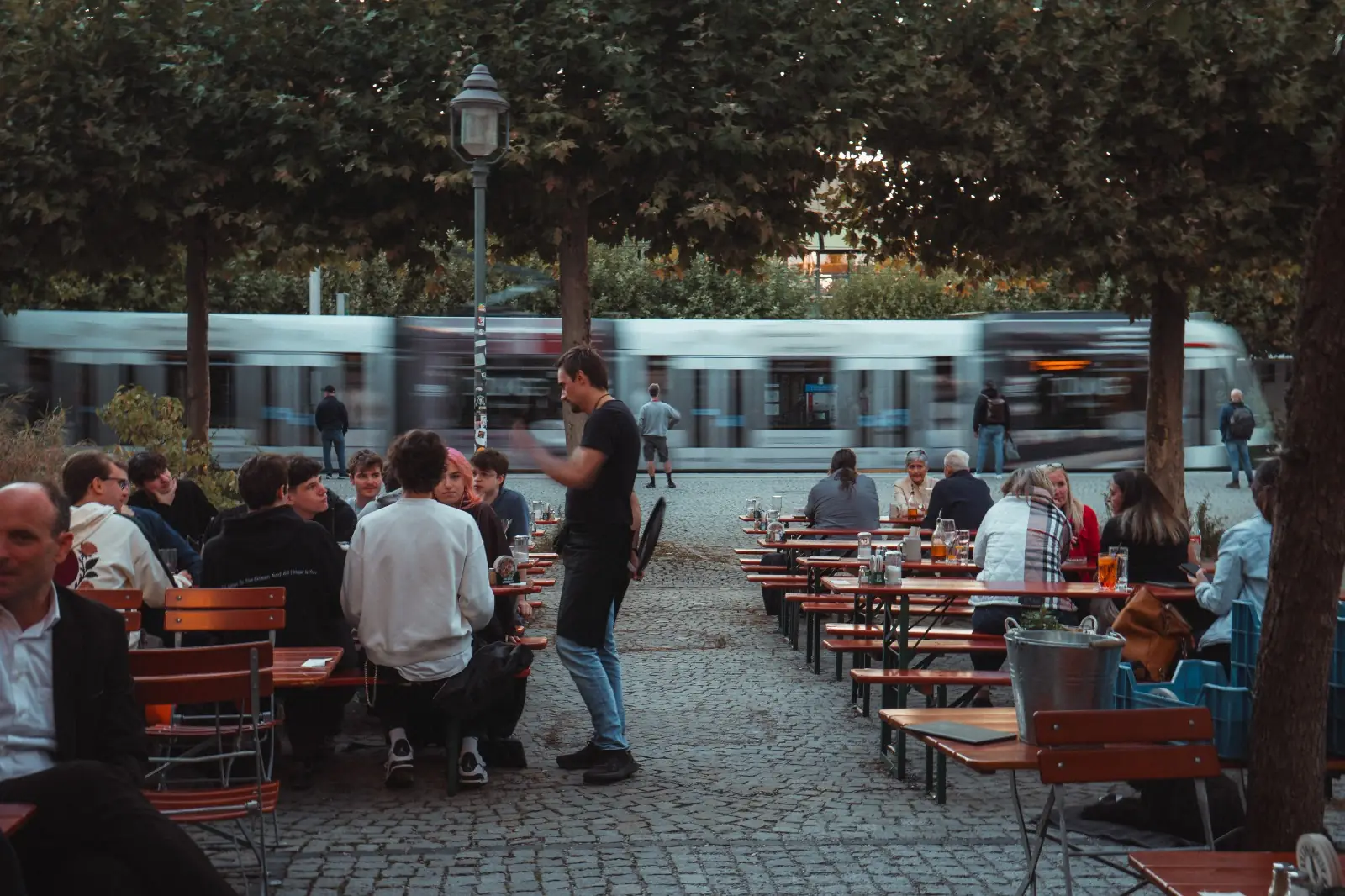 UNIKUM Biergarten mit Gästen und Tram im Univiertel